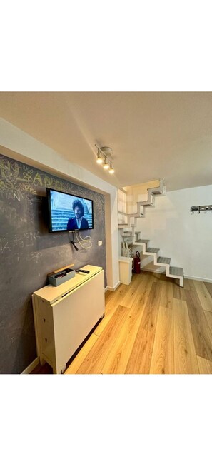 Ein modernes Interieur mit einem Flachbildfernseher an einer Tafelwand, einem weißen Schrank und einer Holztreppe.
