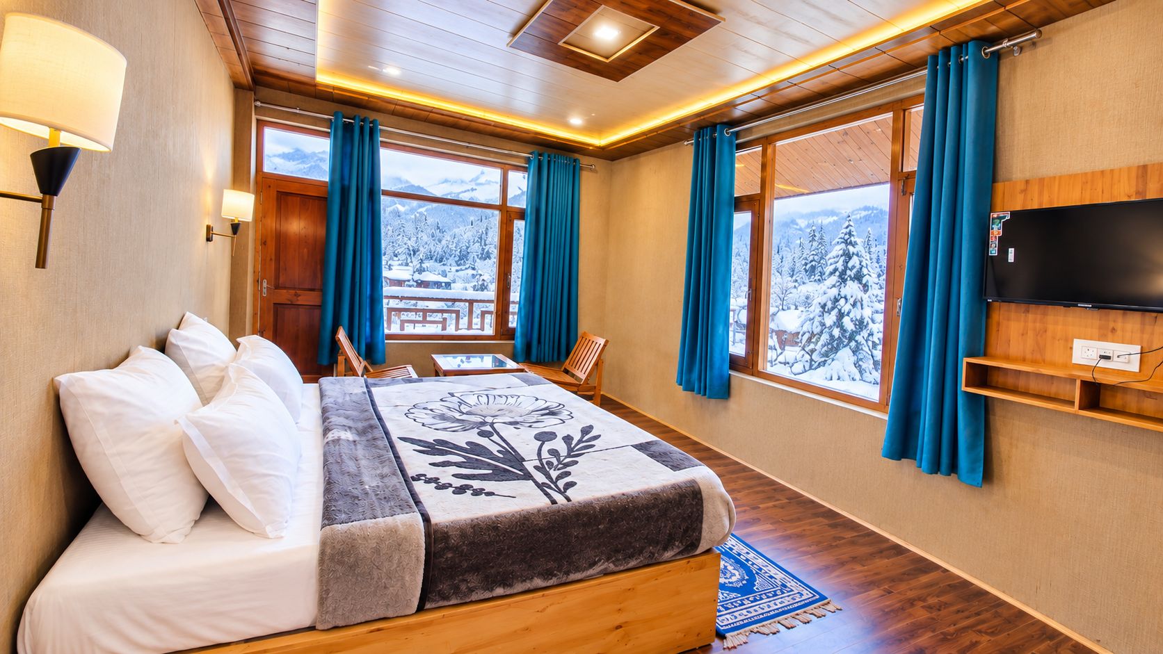 A hotel room with a bed, a television, and a view of snow-covered trees.