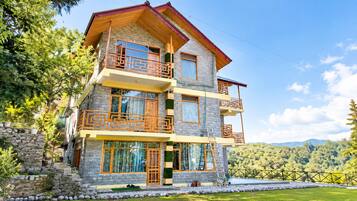 A multi-story building with balconies, stone facade, and a view of a forested area.