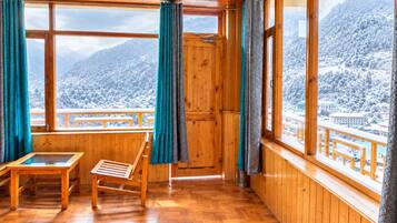 Una habitación de madera con un banco, una mesa y ventanas amplias que ofrecen vistas de montañas nevadas.