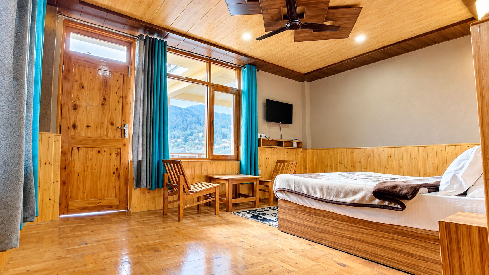 A wooden-floored room with a bed, a desk, and a chair.
