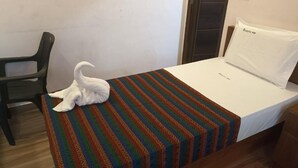 Un llit individual amb un estovat estampat, un almoïna blanca i una cadira negra en una habitació amb una paret sense motius i una porta.