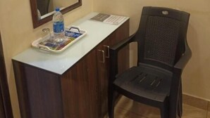 Habitació petita amb escriptori de fusta, una cadira, un mirall gran i una safata amb ampolla d'aigua i revistes.