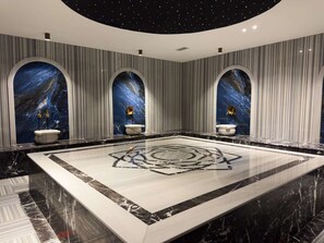 Ein luxuriöses Badezimmer mit großflächigem Marmorboden, drei sturzfeldern mit goldenen Wasserhähnen und einer himmelsartigen Deckenmalerei.