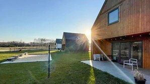 Un bâtiment moderne doté d’une grande porte vitrée, d’un patio avec des chaises et d’une pelouse.