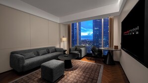 Una habitación de hotel moderna con un ventanal grande, un sofá, una mesita y una pantalla de televisión.