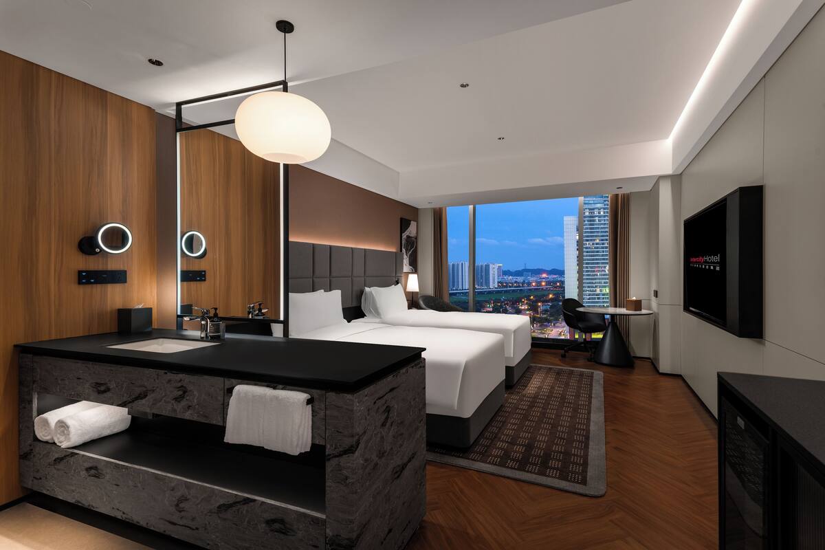 A modern hotel room with a large bed, a separate seating area, a bathroom with a marble vanity, and a city view.