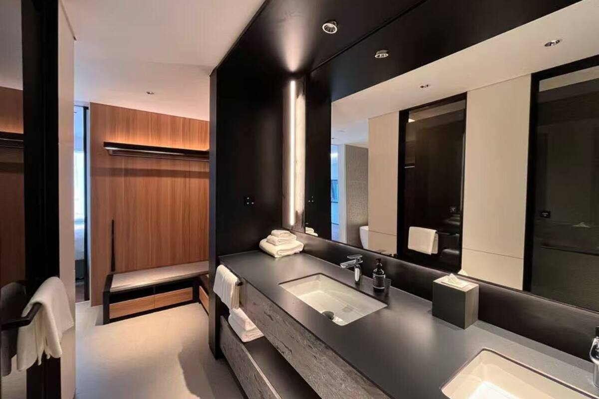 A modern bathroom with a large mirror, two sinks, and a bench.