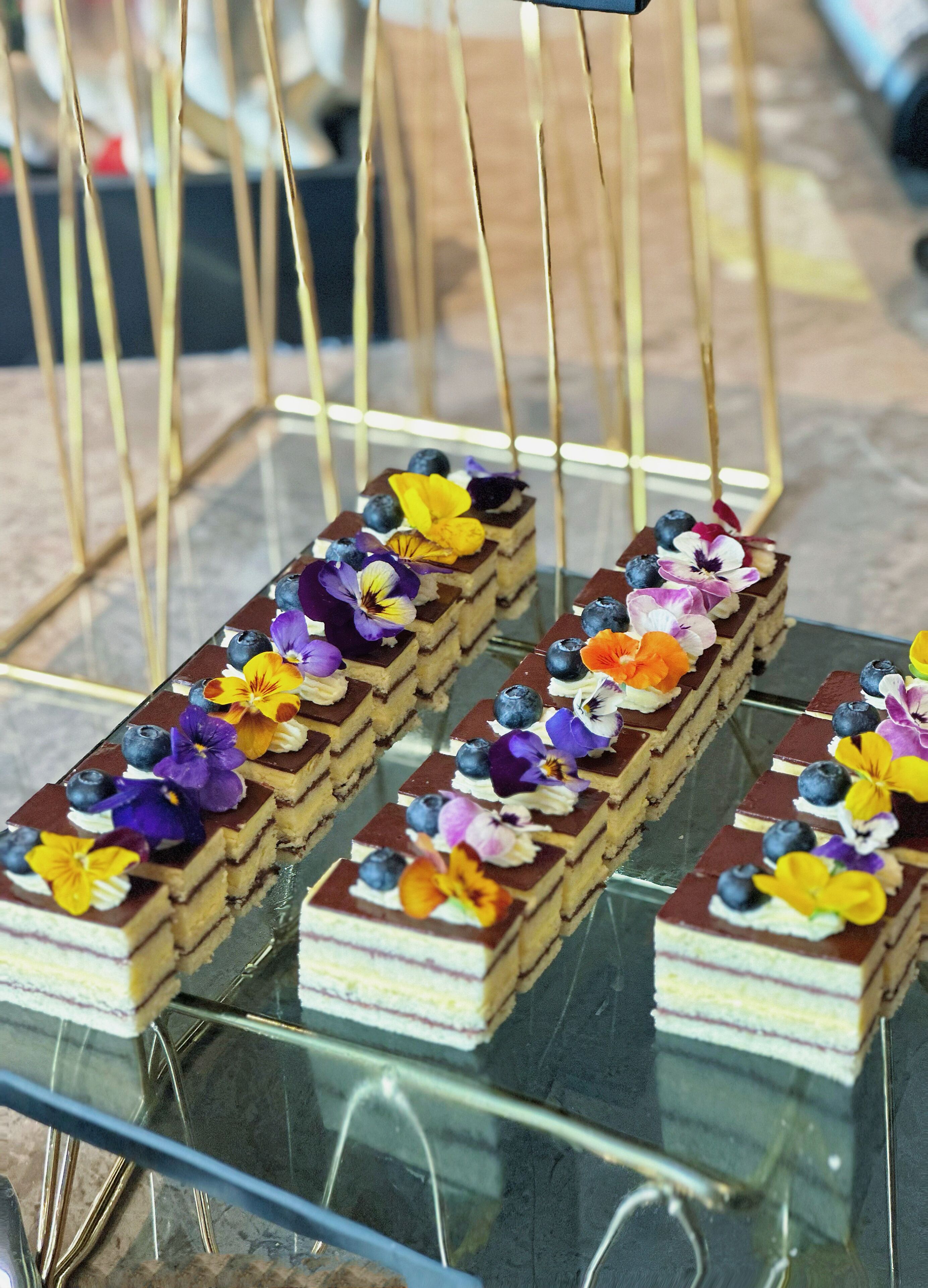 Una bandeja de postres con varios pasteles rectangulares adornados con flores y frutos rojos.