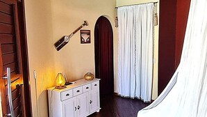 Een kamer met een houten plafond, een wit kastje, een deur en een gordijn.
