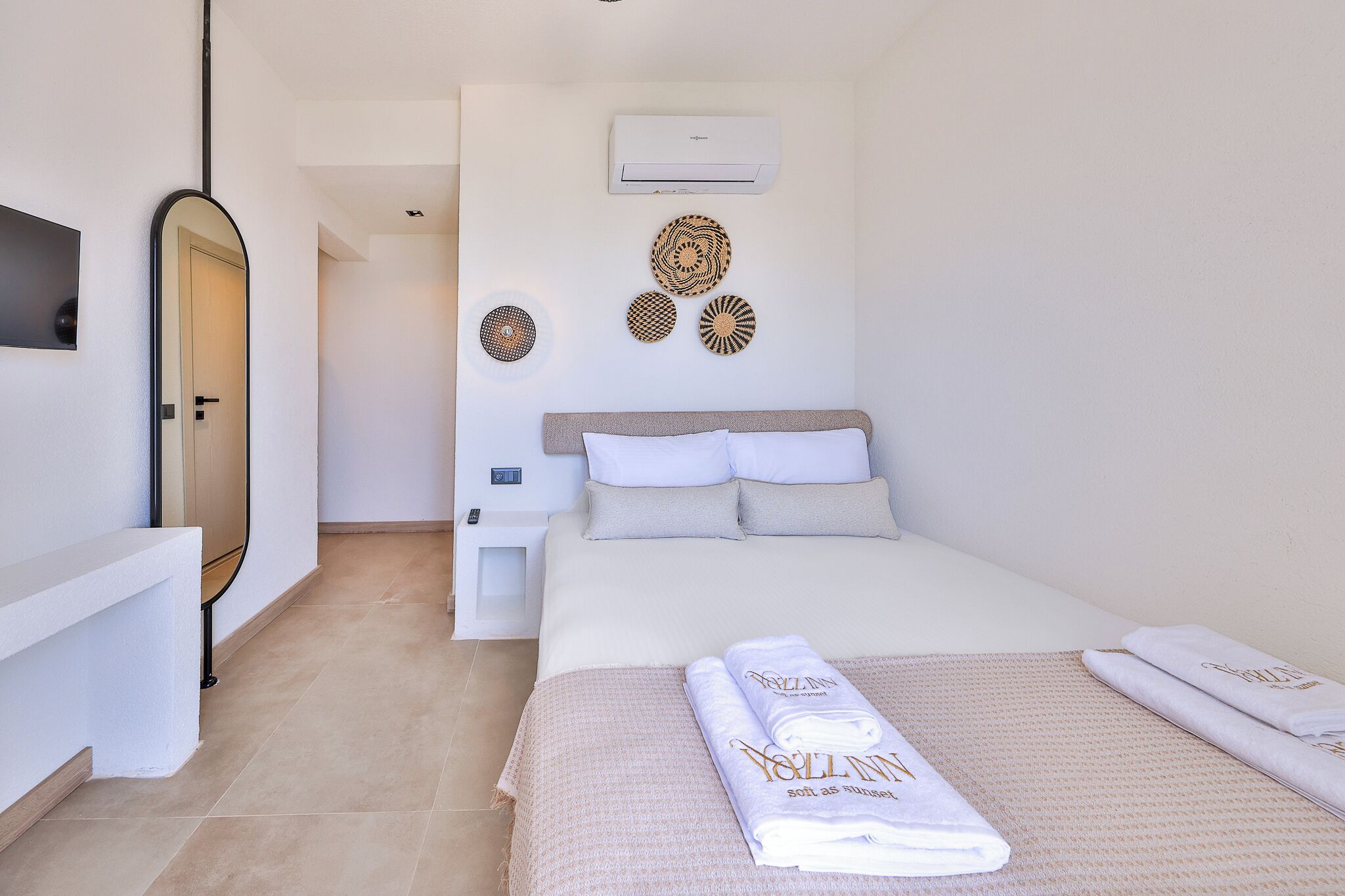 A hotel room with a bed, a bedside table, a mirror, an air conditioning unit, and decorative wall art.
