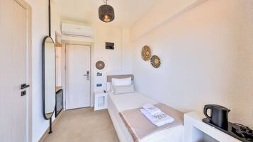 A small, clean room with a bed, a desk, a kettle, and a mirror.