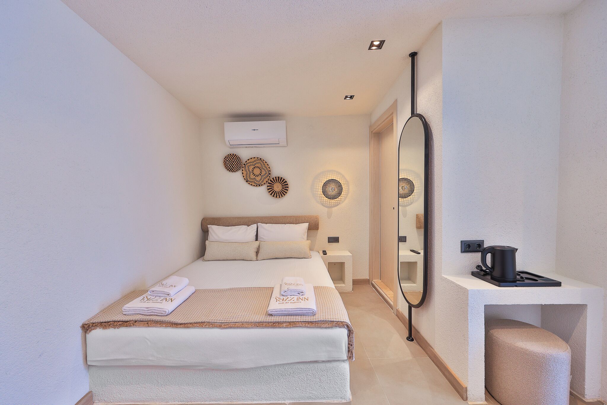 Habitación de hotel con cama, mesitas de noche, un espejo y una cafetera.