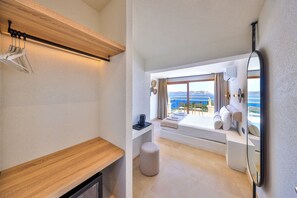 A modern room with a wooden bench, a round ottoman, a bed with a view, a mirror, and a window with curtains.
