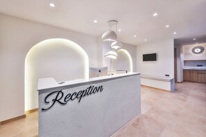 Ein Empfangstresen mit einem Schild mit der Aufschrift 'Reception', ein an der Wand befestigter Flachbildfernseher und eine moderne Pendelleuchte.