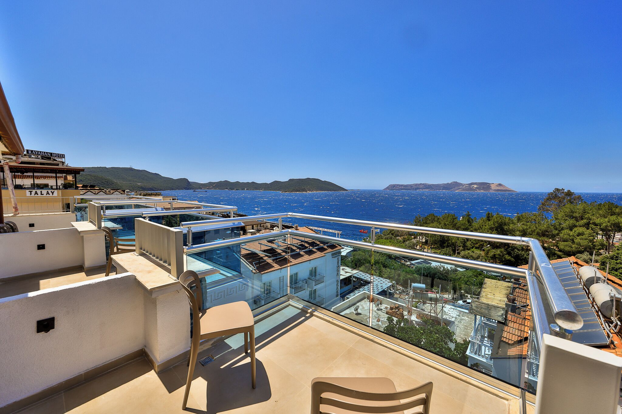 A rooftop terrace with a glass balustrade, outdoor seating, and a view of the sea and distant islands.