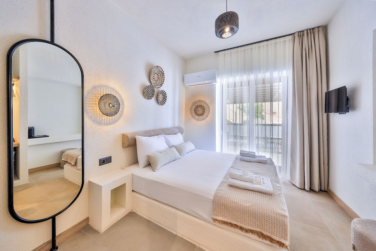A modern hotel room with a large bed, a wall-mounted TV, and a large mirror.
