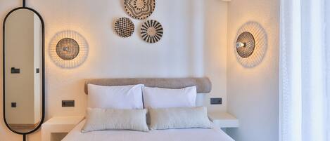 A bedroom with a bed, pillows, a mirror, wall-mounted lights, and an air conditioning unit.