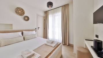 A hotel room with a bed, a desk with a coffee machine, a TV, and a large window with curtains.