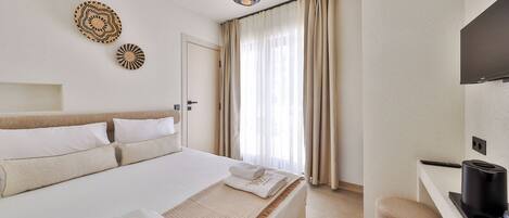 A hotel room with a bed, a desk with a coffee machine, a TV, and a large window with curtains.