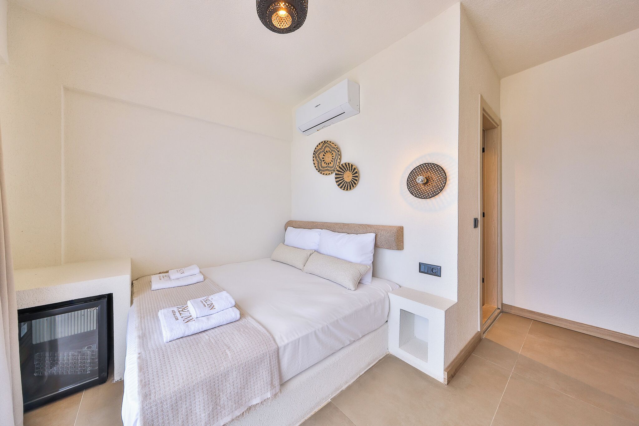A bedroom with a bed, a wall-mounted air conditioner, decorative wall art, a bedside table, and a built-in heater.