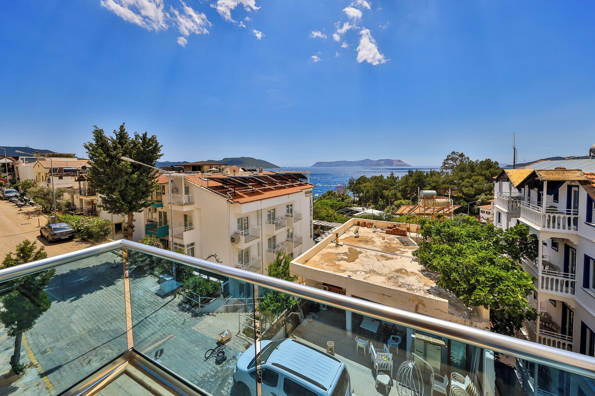 A residential area with a clear view of the sea, a balcony with outdoor furniture, and a building with a partially constructed roof.