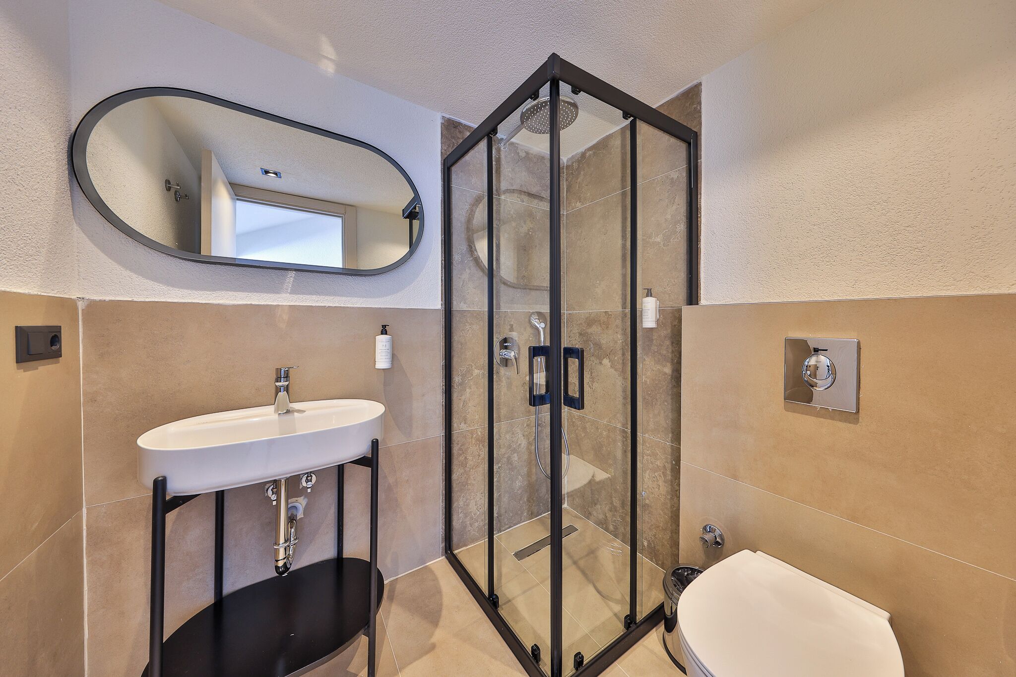 Une salle de bain avec une douche à parois de verre, un lavabo sur un piédestal noir et des toilettes.