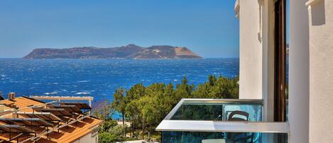 A balcony with a glass railing overlooking a coastal view, a clear sky, and a distant island.