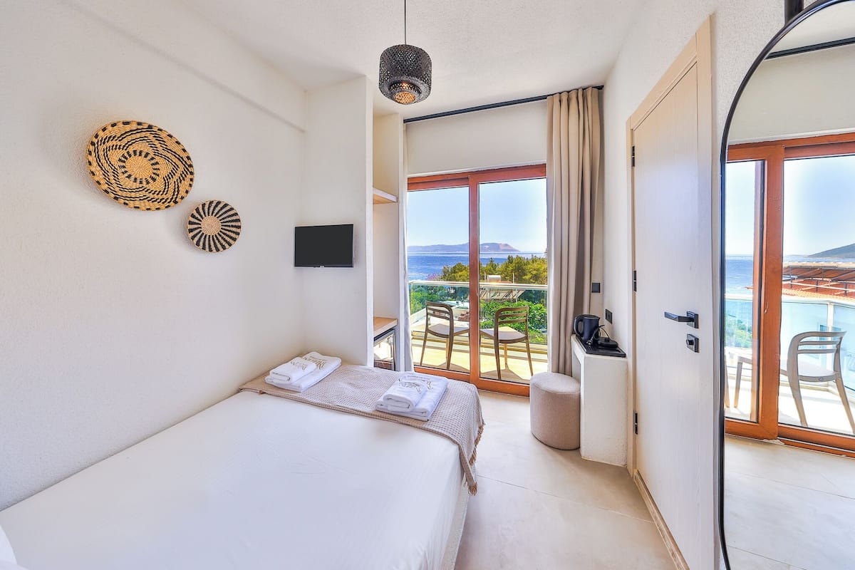 A bedroom with a bed, a television, a view of the outdoors, and a balcony with chairs.