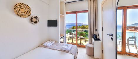 Un dormitorio con cama, televisión, vistas al exterior y un balcón con sillas.