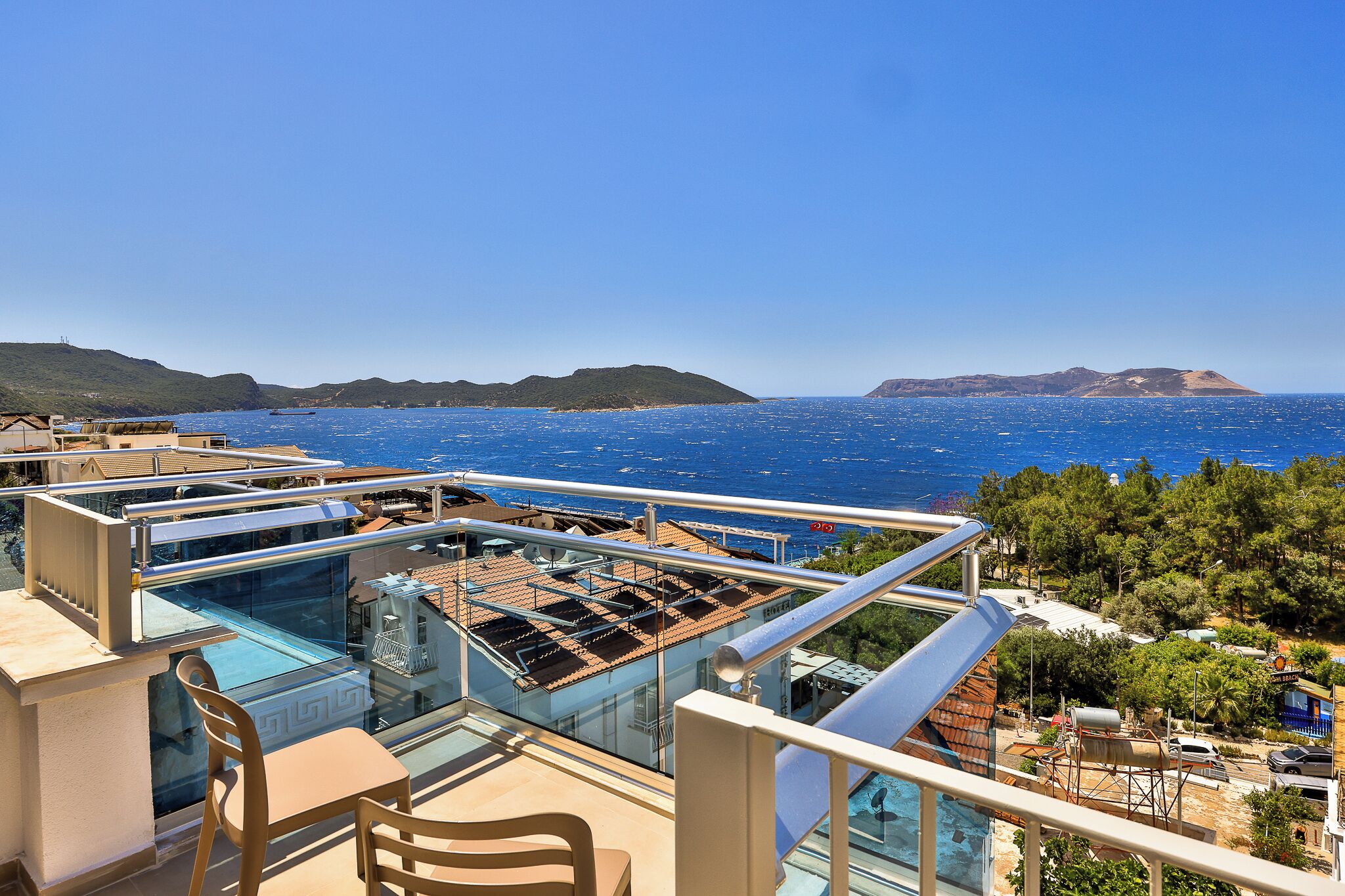 Eine Dachterrasse mit Glasbrüstung, einem Pool und Blick auf das Meer und die Hügel.