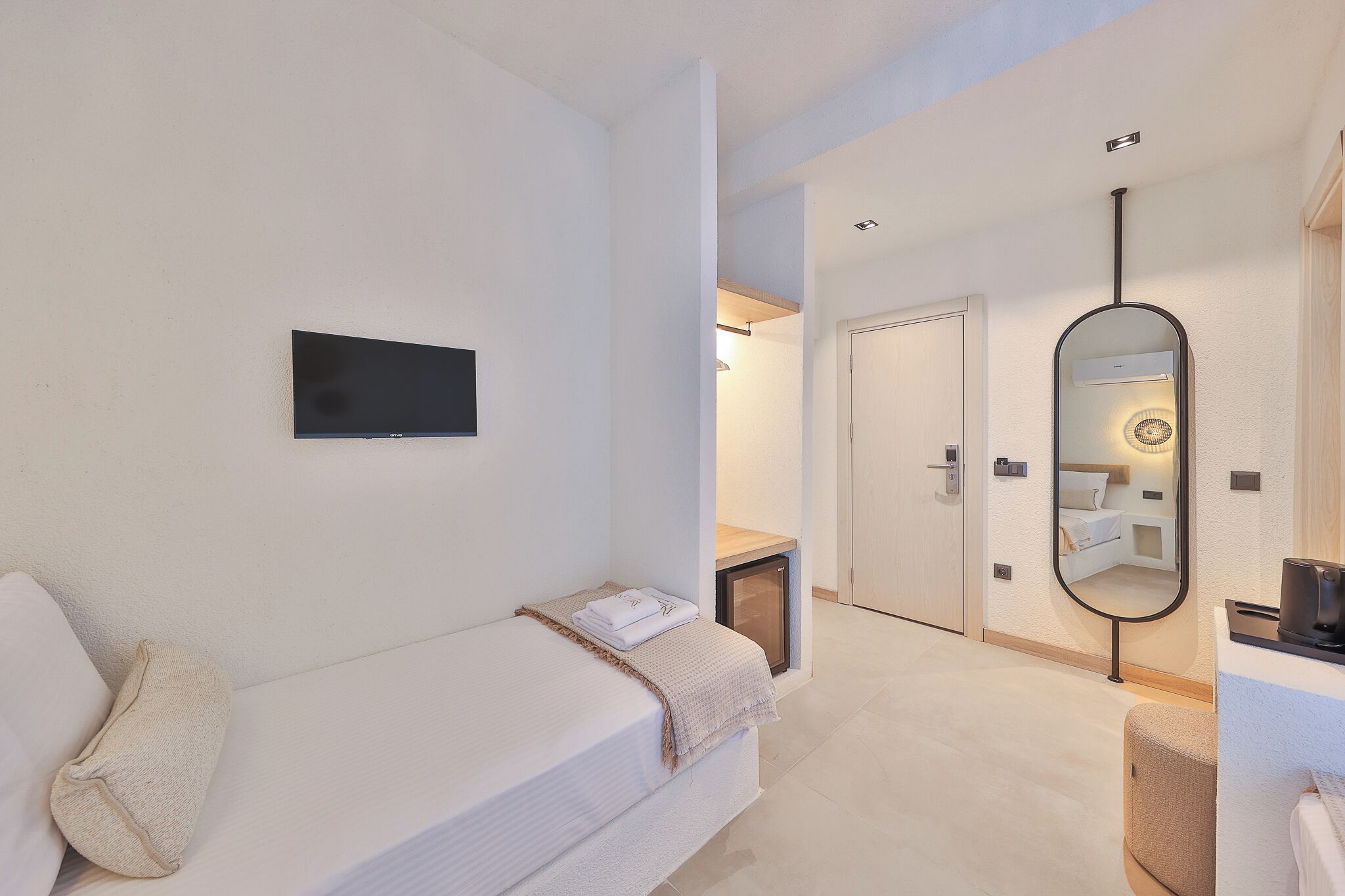 A hotel room with a bed, a TV, a mirror, and a door leading to another room.