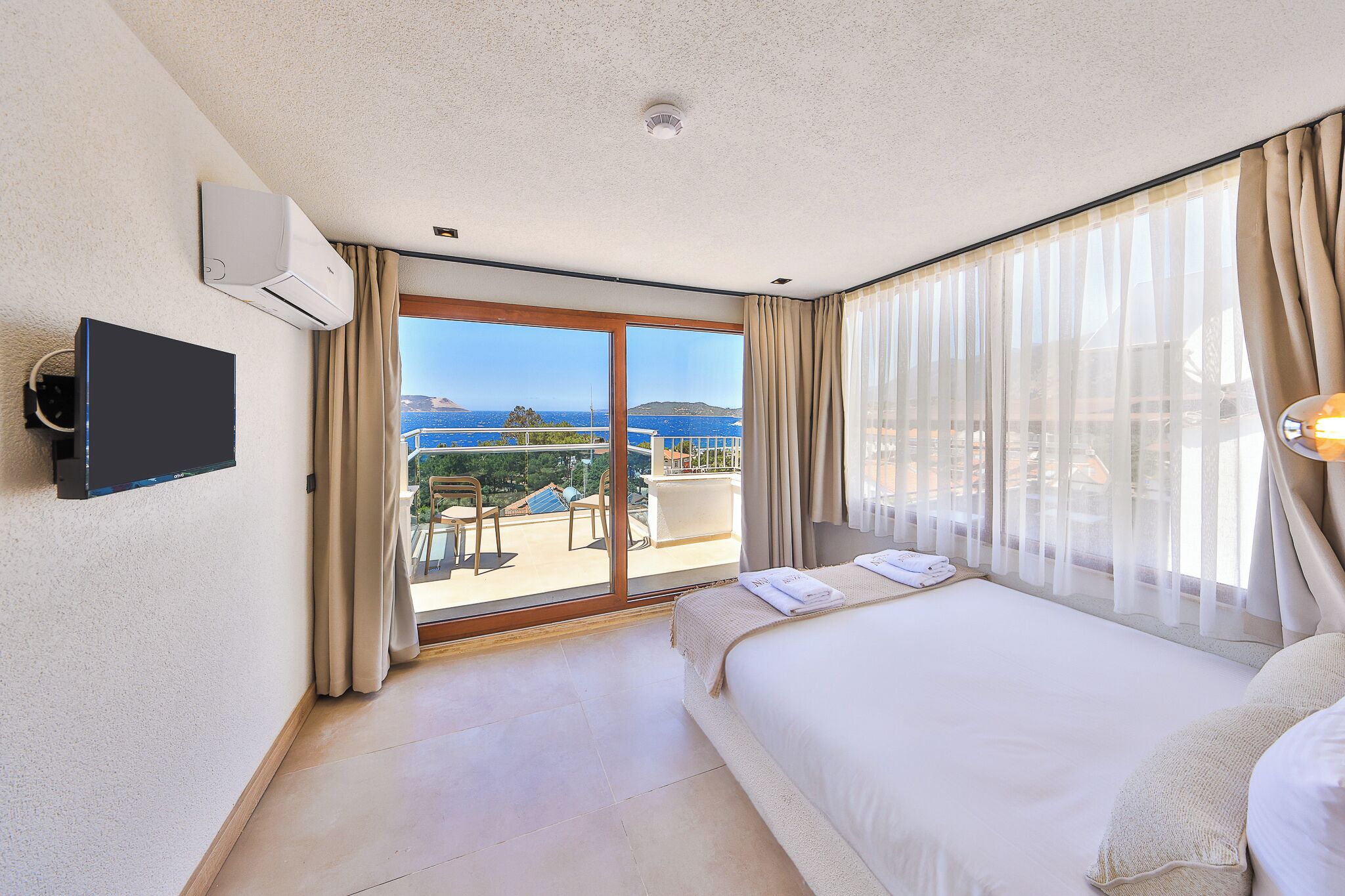 A hotel room with a bed, a TV, a balcony with a view, and an air conditioning unit.