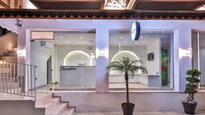 A hotel entrance with a reception desk, a staircase, and potted plants.