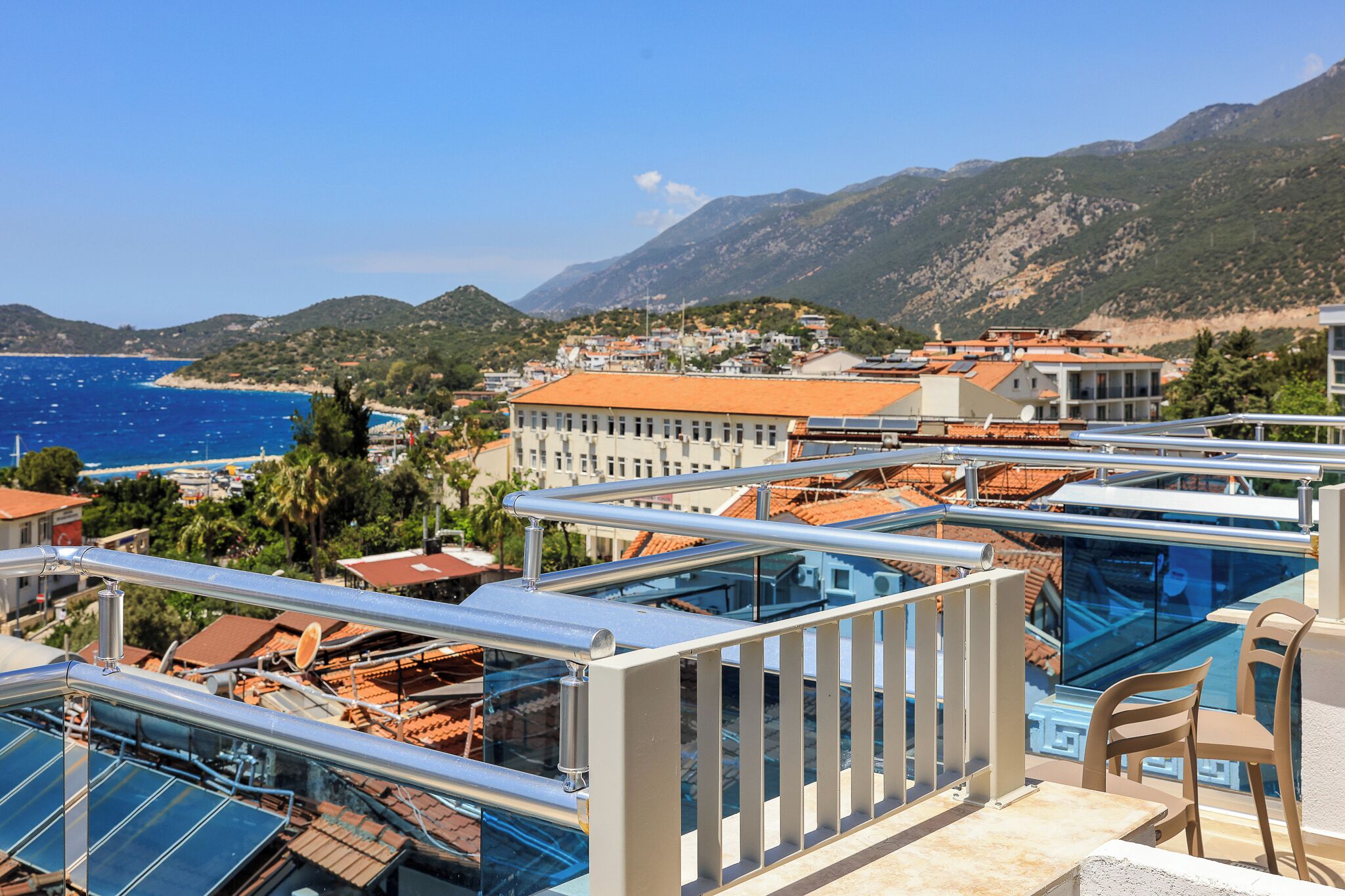 A coastal hotel with balconies, solar panels, and a view of the sea and mountains.