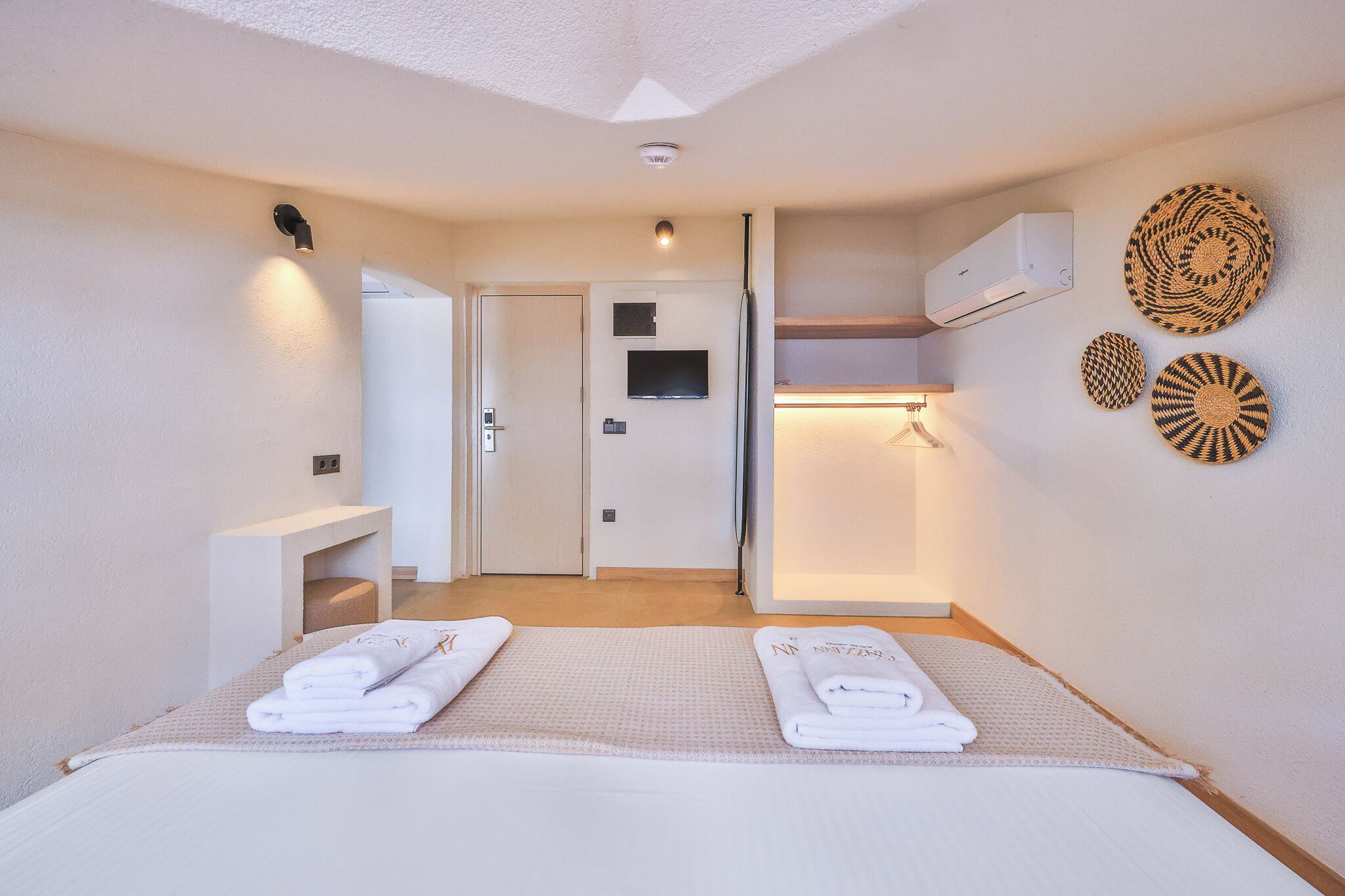 A hotel room with a bed, a TV, a wall-mounted air conditioner, and a door leading to another room.