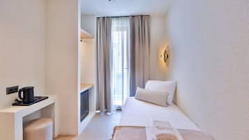 Une chambre d’hôtel avec un lit, un bureau doté d’une bouilloire, une lampe fixée au mur et une fenêtre avec des rideaux.