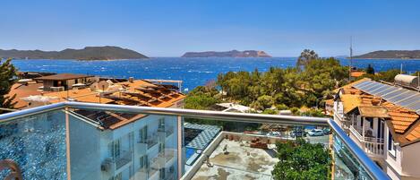 A balcony with a glass barrier overlooking a coastal area with buildings and a clear sky.