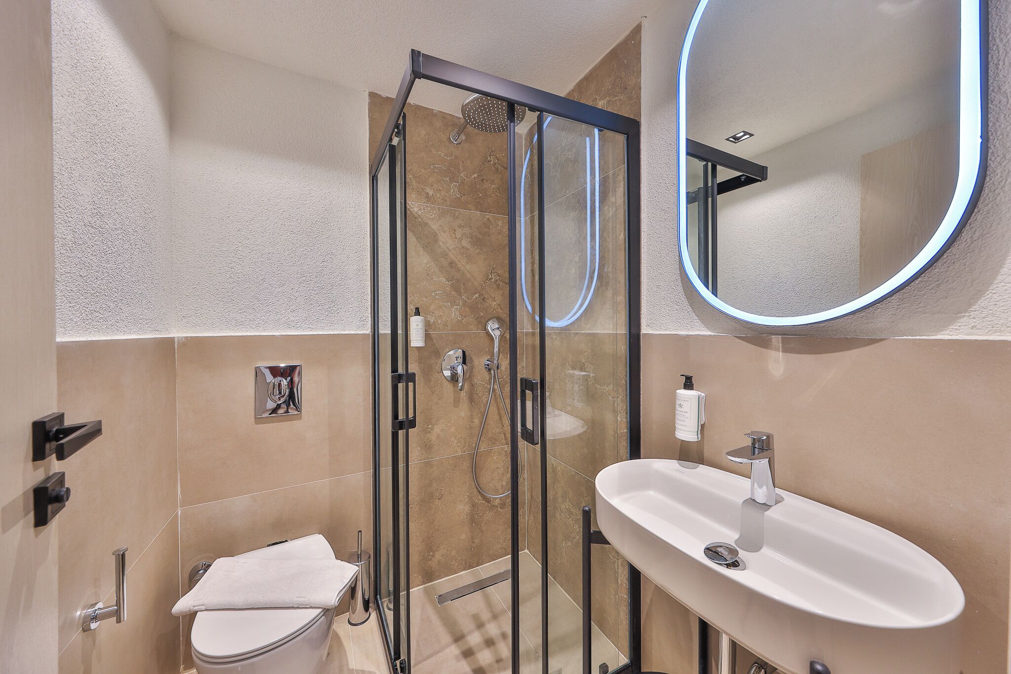 Un baño moderno con ducha de vidrio, lavamanos blanco y un espejo grande.