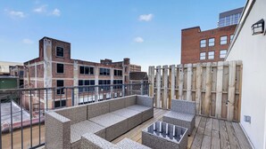 Eine Dachterrasse mit Korbmöbeln, einer Holzterrasse und Blick auf umliegende Gebäude.