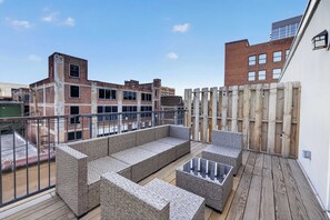 Eine Dachterrasse mit Korbmöbeln, einer Holzterrasse und Blick auf umliegende Gebäude.