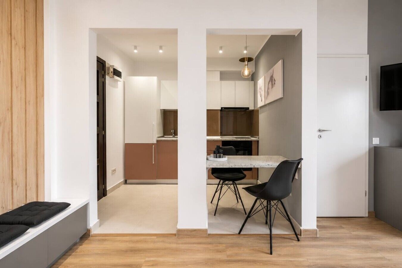 A modern kitchen with a dining area, wooden flooring, and a TV mounted on the wall.