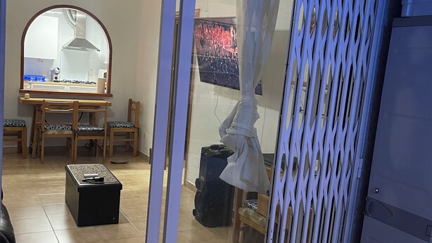 Ein Zimmer mit einer Schiebetür und direktem Zugang zu einer Küche, einem Essbereich mit Tisch und Stühlen sowie einer kleinen Sitzecke mit Sessel und Tisch.