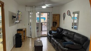 Ein Wohnzimmer mit einer Ledersofa, einem Fernseher, einem Deckenventilator und Blick durch eine Glastür.