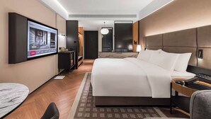 A modern hotel room with a large bed, a flat-screen TV mounted on the wall, a desk with a chair, and a small table. - Songshan Lake Intercity Hotel (Dongguan)