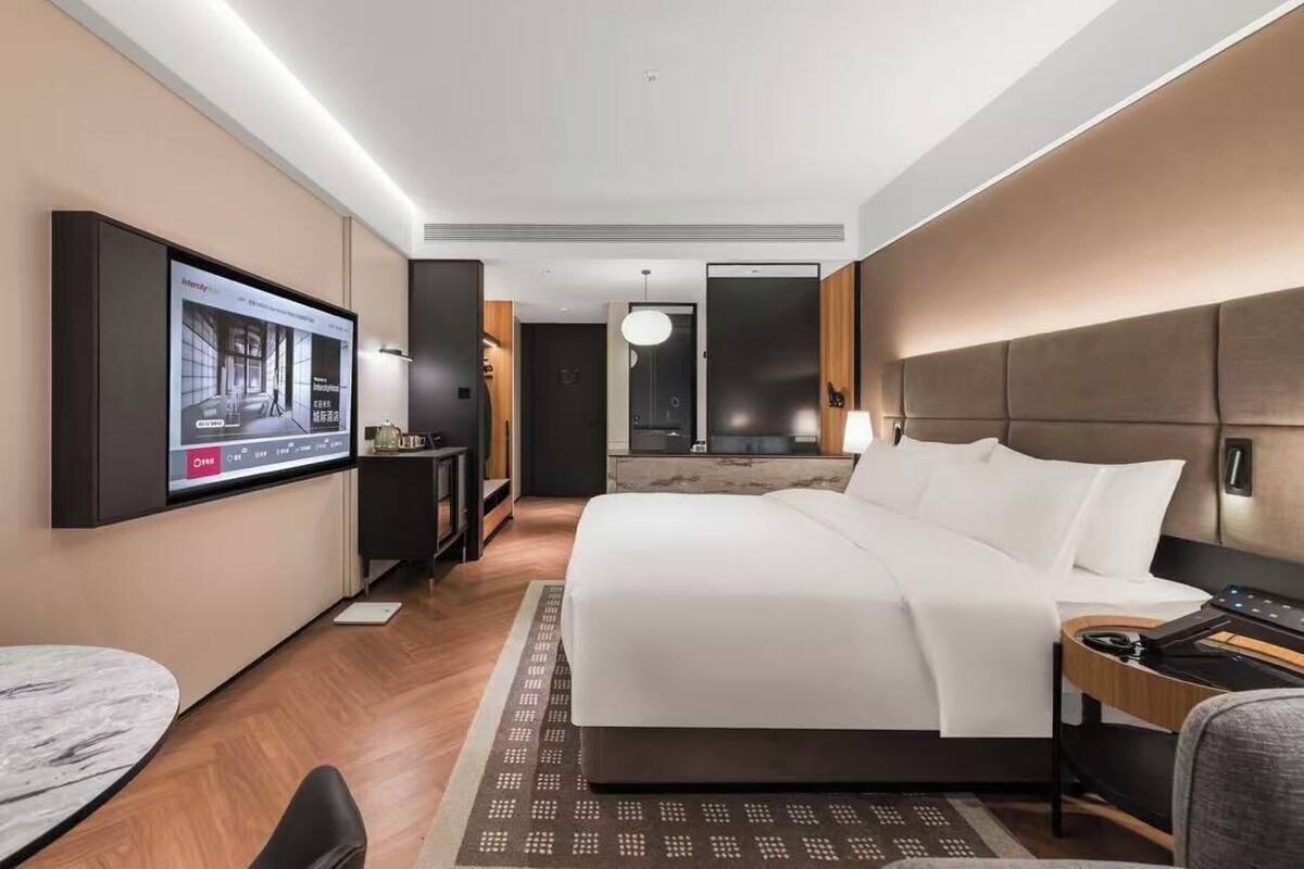 Una habitación de hotel moderna con una cama grande, un televisor de pantalla plana montado en la pared, un escritorio con una silla y una mesita.