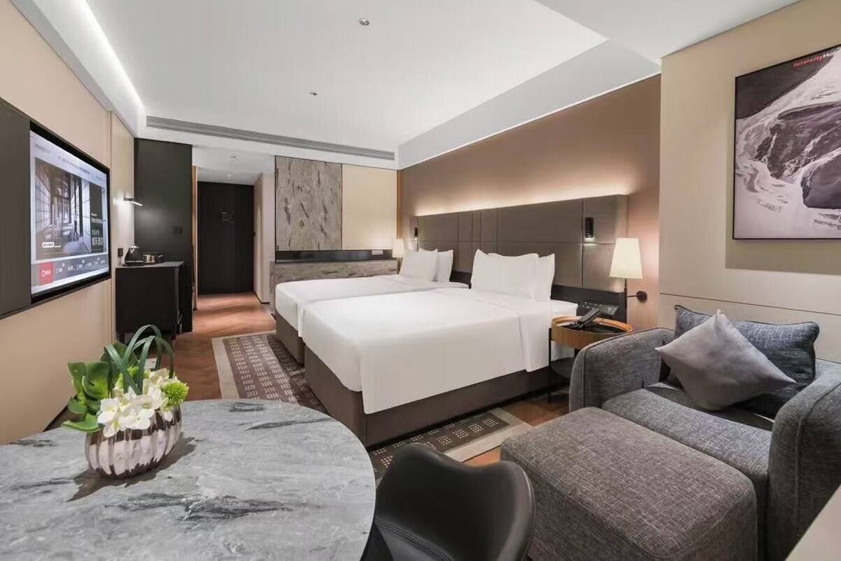 Habitación de hotel con una cama grande, un escritorio, una silla, un televisor y una obra de arte colgada en la pared.