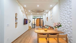 A modern interior with a wooden dining table, chairs, a sofa, and a staircase. - Hometown Nimi 3 BRS Pool Villa Da Nang (Da Nang)