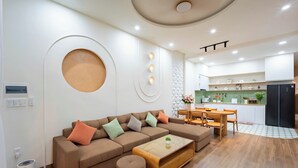 A modern living room with a sectional sofa, a coffee table, and a dining area with chairs and a table. - Hometown Nimi 3 BRS Pool Villa Da Nang (Da Nang)