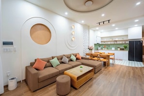 A modern living room with a sectional sofa, a coffee table, and a dining area with chairs and a table. - Hometown Nimi 3 BRS Pool Villa Da Nang (An Hai)